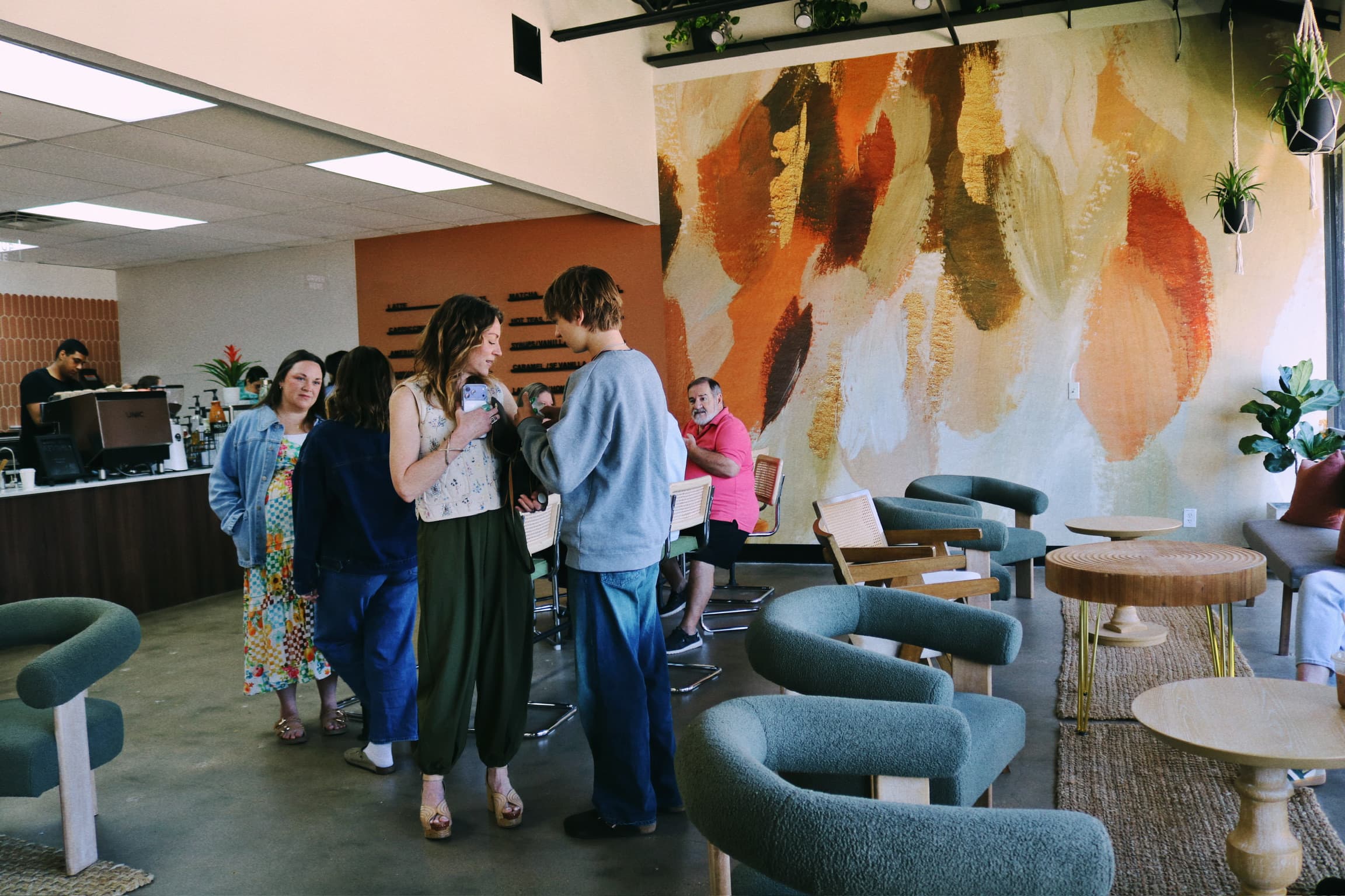 Customers laughing together near the Revival Coffee counter with the orange-and-cream mural in the background